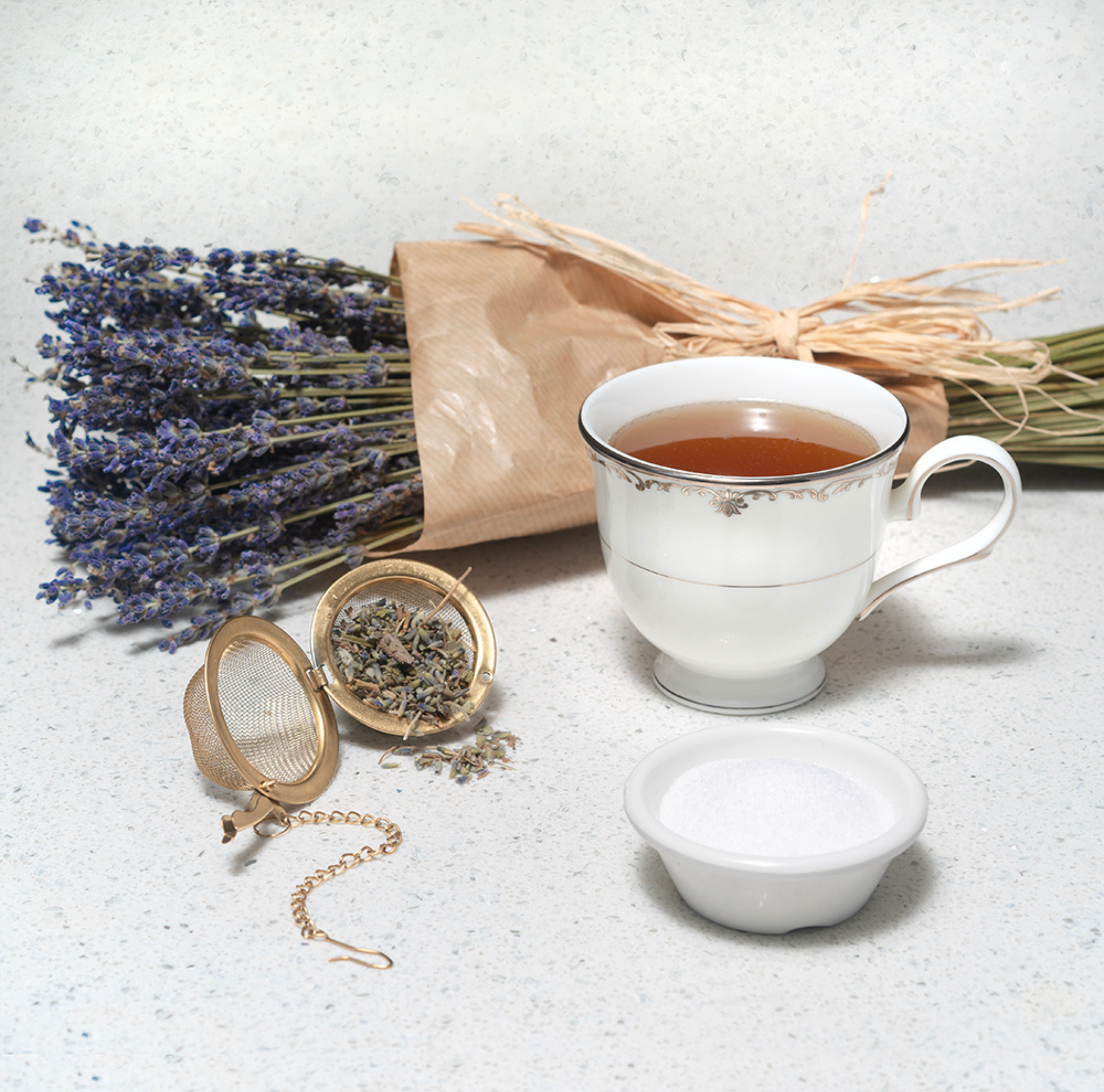 Image of lavender stock and tea infuser next to tea in porcelain teacup on white background